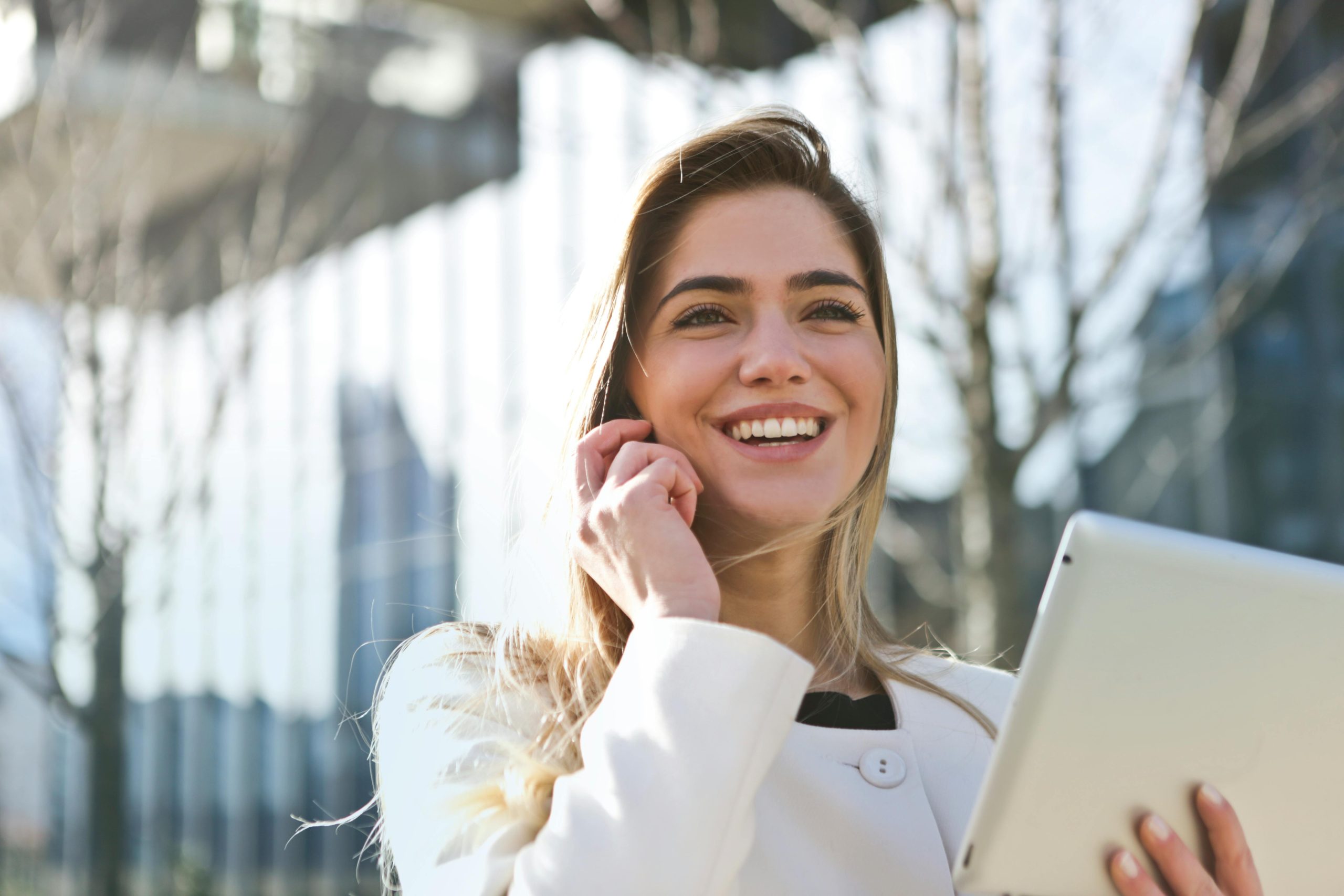 Confident businesswoman using her tablet and phone, smiling outdoors in sunlight. Social Media.