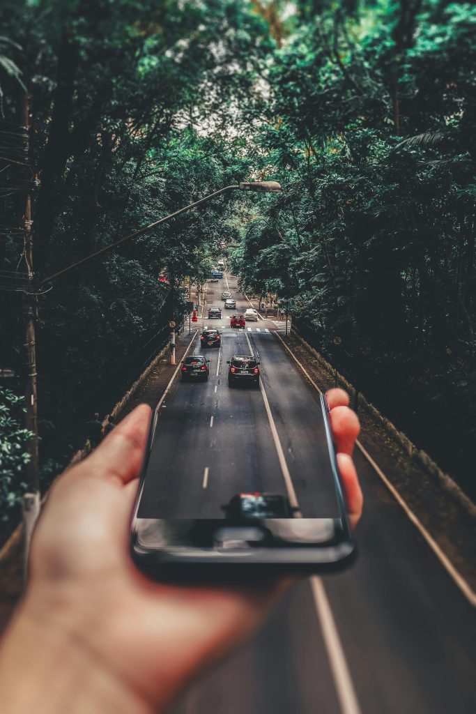 Creative blend of technology and nature with smartphone framing a bustling road through forest. Social Media.